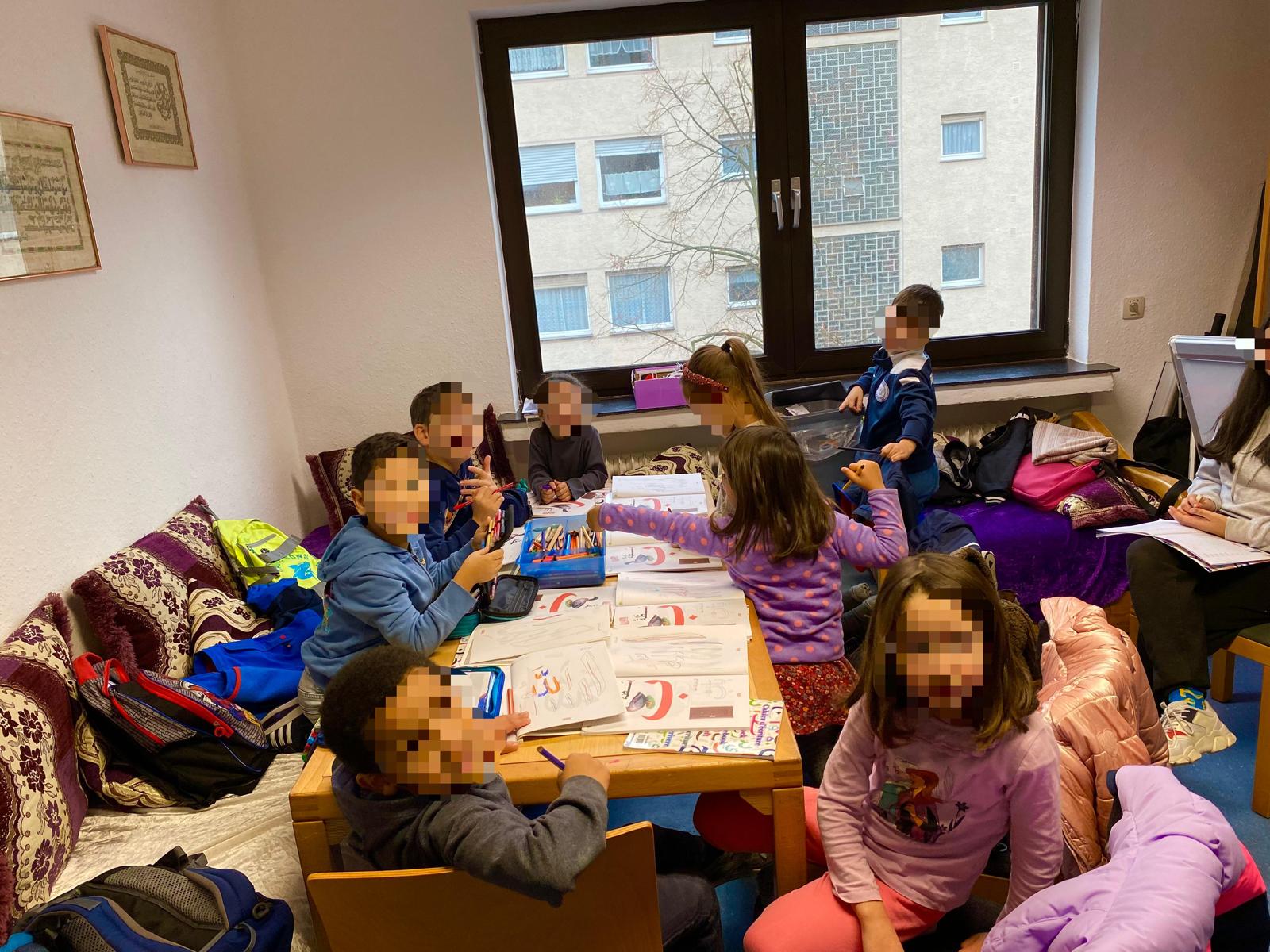 Kinder bearbeiten im Iman Zentrum gemeinsam am Tisch Arbeitsblätter mit arabischen Buchstaben