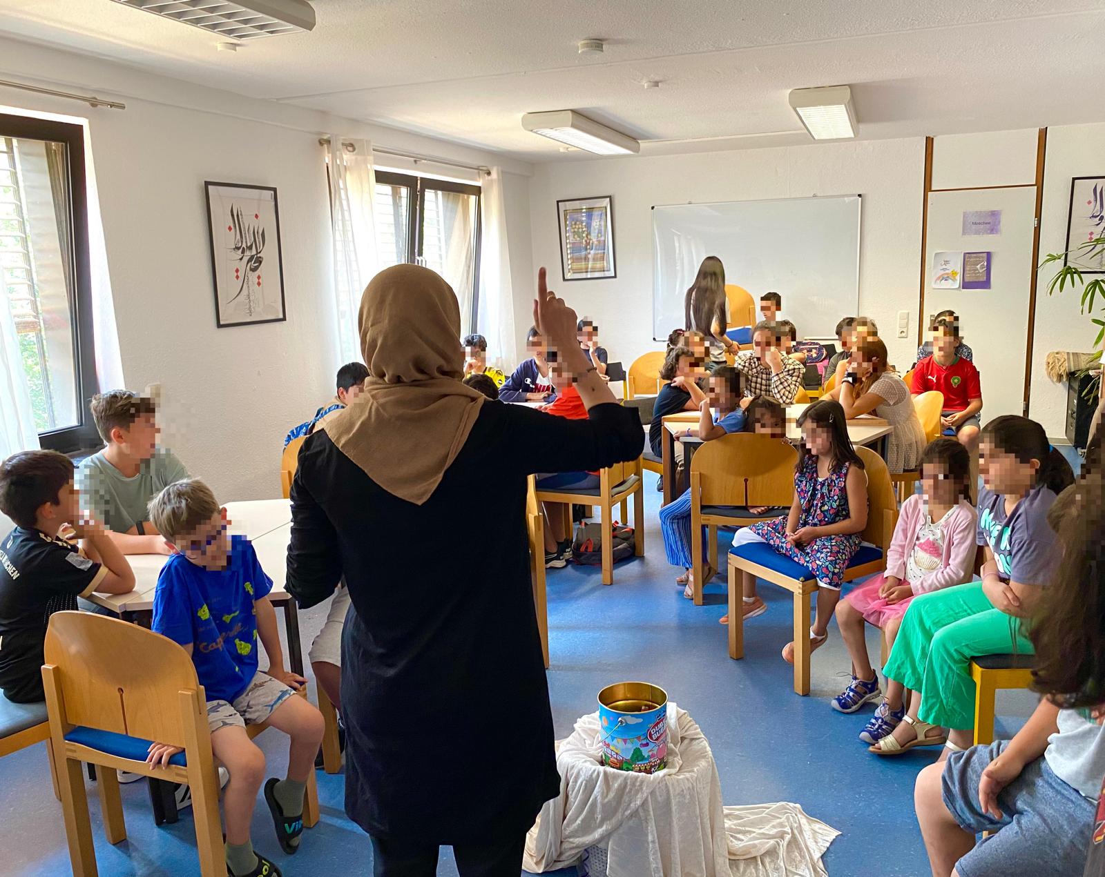 Lehrerin erklärt einer Kindergruppe etwas, an der Wand hängt arabische Kalligrafie